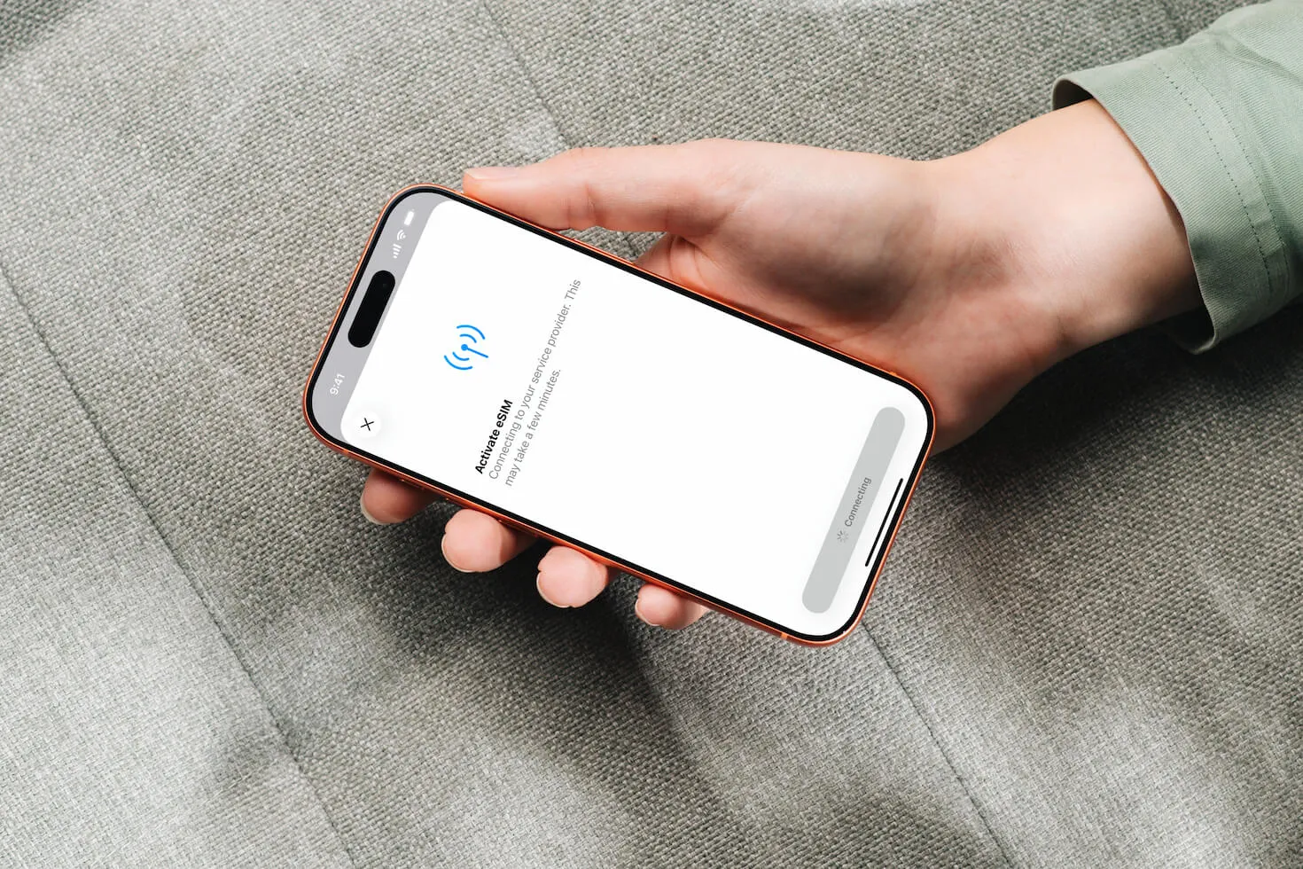 A hand holding an iPhone showing the iOS 'Activate eSIM' screen — connecting to the service provider.